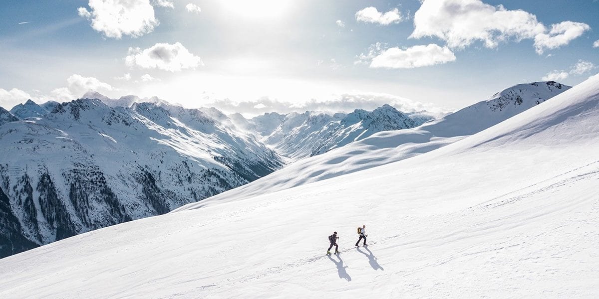 herring-group-pleased-satisfied-alpine-climb-1200×600-min-1200×600-min 2 people enjoying a winter hike on a snow covered mountain.